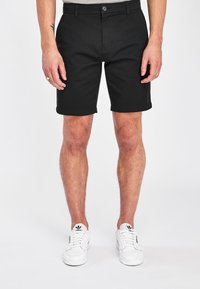 Shorts negri dintr-o țesătură din bumbac, având un design cu față plată, închidere cu nasture și buzunare laterale. Marginile sunt tivite, iar croiala este ajustată.