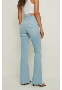 Jeans svasati di un blu chiaro realizzati in denim, con vita alta, tasche posteriori e un'etichetta marrone del marchio sulla vita.