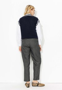 Top sans manches en tricot bleu marine, chemise blanche en dessous, pantalon à motifs carreaux gris et ballerines imprimé léopard.