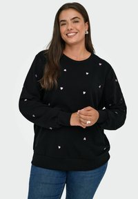Schwarzer Sweatshirt mit verstreuten kleinen rosa Herzmustern, Rundhalsausschnitt und gerippten Bündchen. Getragen mit blauen Jeans.