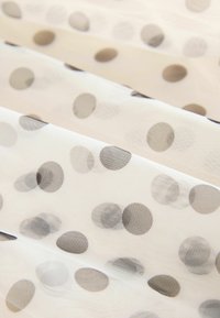 Przezroczysty materiał o kremowym tle z rozproszonymi czarnymi kropkami w różnych rozmiarach, tworzący teksturowany, warstwowy wygląd.