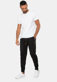 Witte katoenen t-shirt gecombineerd met zwarte joggingbroek met oranje trekkoord en een klein logo, aangevuld met witte sneakers.