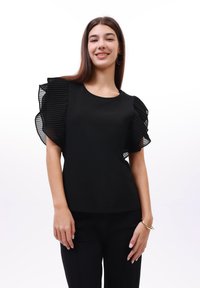 Černý top s krátkými, volánkovými průhlednými rukávy, kulatým výstřihem a klasickým střihem. Hladká textura a jednoduchý design.