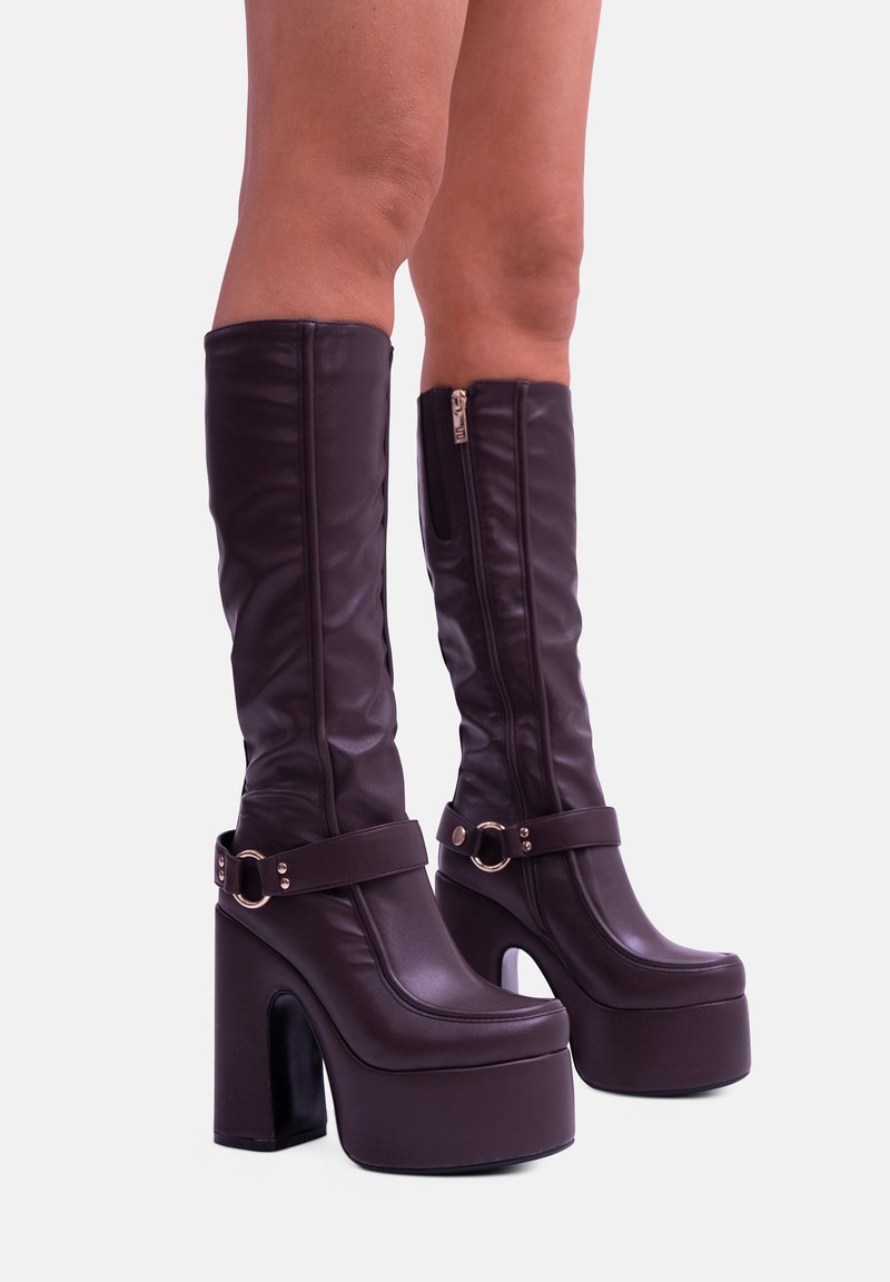 Stivali alti fino al ginocchio in finta pelle marrone con platform e tacco spesso, dotati di una zip laterale e di una cinghia regolabile con dettagli in metallo.