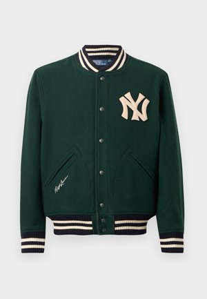 Casaco varsity verde escuro com punhos e colarinho listrados, botões de pressão, logotipo dos New York Yankees no peito e assinatura de Ralph Lauren perto do bolso.
