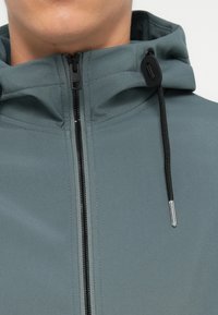Hoodie aus weichem grauen Stoff mit vollem Reißverschluss, ausgestattet mit schwarzen Kordeln und metallischen Akzenten an der Kapuze und dem Reißverschluss.