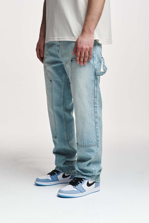 Light blue denim cargo pants with multiple pockets, loose fit, and stitched detailing, paired with black and blue sneakers.