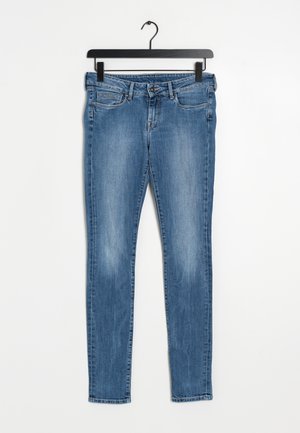 Jeans in denim blu su un appendiabiti nero, con una vestibilità slim, leggermente sbiaditi, cinque tasche e chiusura con zip.