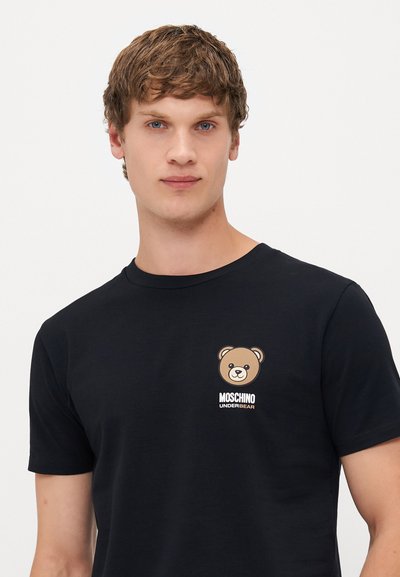 Camisa de t-shirt preta de mangas curtas feita de algodão. Apresenta um gráfico de urso e o texto "MOSCHINO UNDERBEAR" no lado esquerdo do peito. Textura suave.