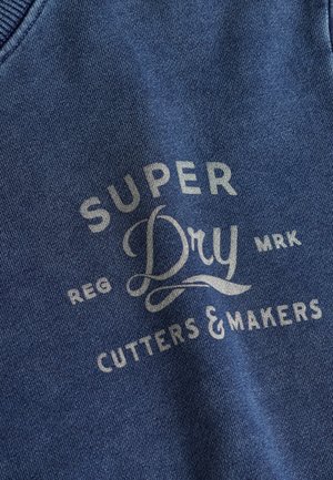 Blauwe stoffen sweatshirt met reliëftekst: "SUPER Dry," "REG," "CUTTERS & MAKERS" in lichtgrijze letters met decoratieve accenten.
