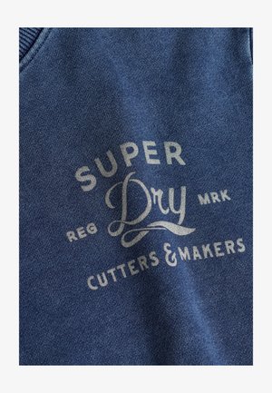 Blauwe stoffen sweatshirt met reliëftekst: "SUPER Dry," "REG," "CUTTERS & MAKERS" in lichtgrijze letters met decoratieve accenten.