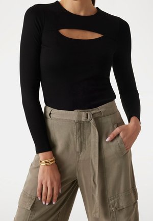 Nainen, joka pukeutunut mustaan pitkähihainen paitaan, jossa on rintaleikkaus, yhdistettynä korkeavyötäröisiin beigeihin cargo-housuihin, joissa on kankainen vyö.