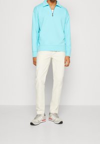 Felpa chiusa azzurra, pantaloni bianchi e scarpe da ginnastica grigie con dettagli rosa. Design semplice, texture morbida e vestibilità casual.