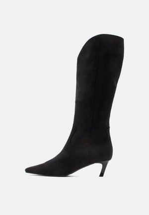 Bottes noires en daim montant jusqu'au genou, avec un bout pointu et un talon bas. Texture lisse, design élégant, avec une ouverture incurvée sur le dessus et sur les côtés.