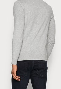Light gray knit sweater with long sleeves and a ribbed hem, shown from the back, paired with dark denim jeans featuring back pockets.