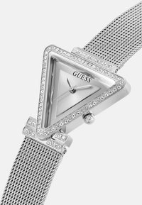 Trekantet sølvur med mesh-rem. Har en krystal-accenteret bezel, sølv urkasse og slanke timemarkører og minutthånd.