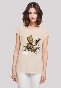 Beige cotton t-shirt featuring a colorful Groot graphic, holding a cassette tape with tangled wires. Round neckline and short sleeves.