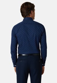 Granatowa koszula z długim rękawem, ozdobiona czerwonym wzorem w kropki, z kołnierzykiem na guziki i białymi guzikami. Gładka tkanina o dopasowanym kroju.