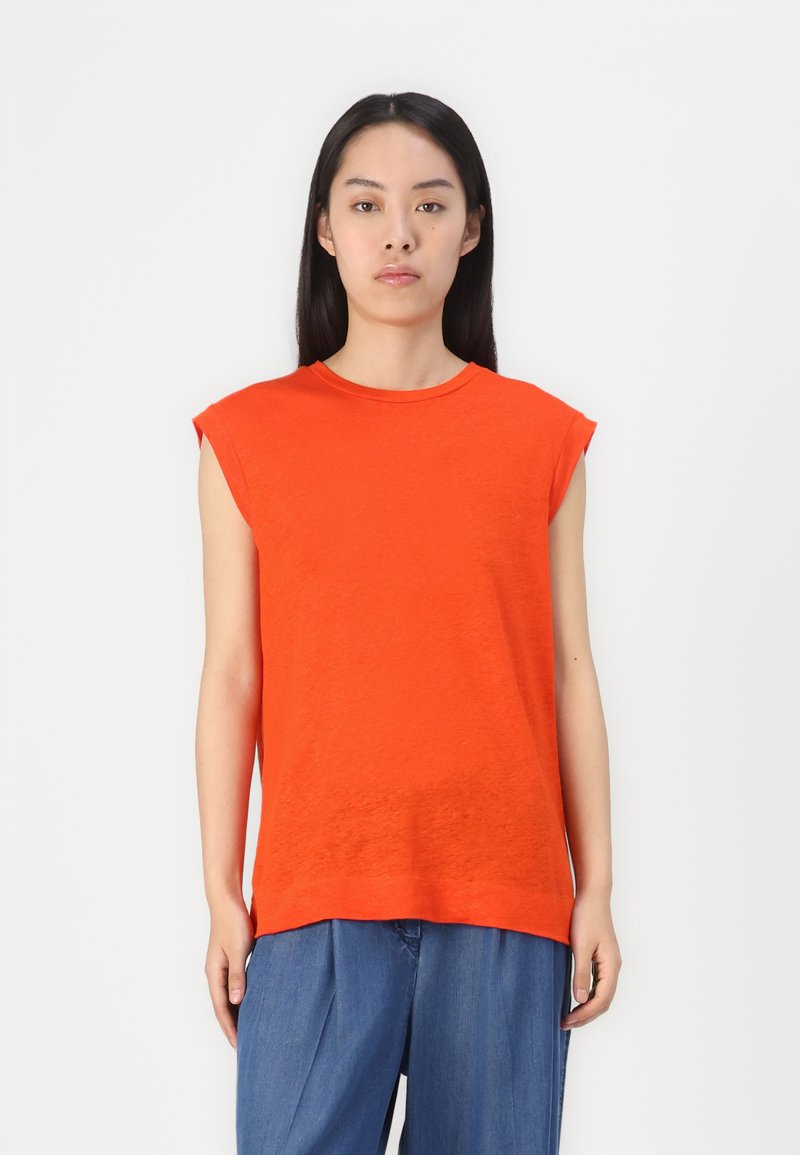 Haut sans manches orange vif avec un col rond et une texture douce. Associé à un pantalon en denim bleu ample. Le fond est blanc uni.
