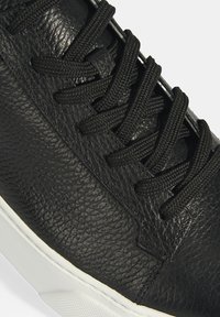 Schwarze Ledersneaker mit strukturiertem Obermaterial, runder Spitze und schwarzen Schnürsenkeln. Weiße Gummisohle mit dezenten Details an der Ferse.