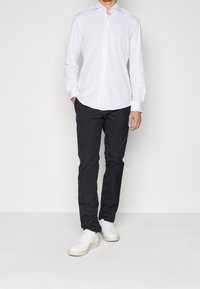 Witte overhemden met lange mouwen. Zwarte slim-fit broek, gladde textuur. Witte sneakers, vetersluiting. Eenvoudige en strakke esthetiek.