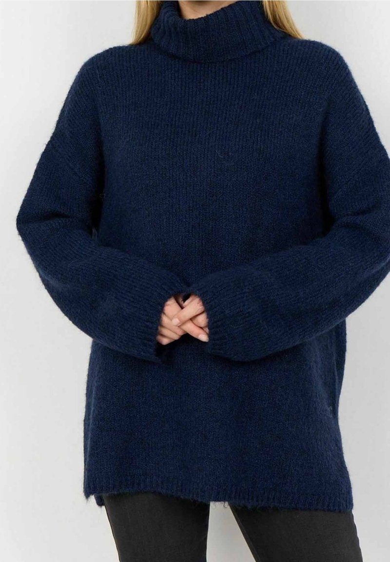 Pull à col roulé tricoté bleu marine avec une coupe décontractée, épaules tombantes et poignets côtelés. Texture douce et fentes latérales à l'ourlet.