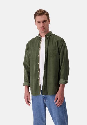 Camicetta verde con bottoni e tasca frontale, design con colletto, tessuto morbido e maniche arrotolate, abbinata a jeans in denim azzurri chiari.