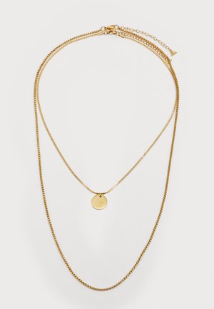 Zlatý tónovaný náhrdelník s vrstvami, který obsahuje tři řetízky různých tlouštěk, z nichž jeden má kulatý přívěsek, hladký povrch a minimalistický design.