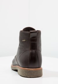 Botas de tobillo de cuero marrón con un acabado texturizado, punta redonda y suela marrón contrastante. Presentan una cinta para tirar y una marca de impermeabilidad.