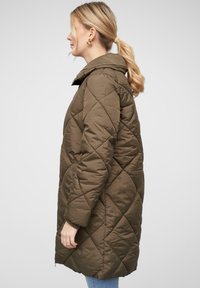 Veste olive matelassée avec capuche, présentant un motif en losanges, des poches latérales et des poignets côtelés, vue de côté.