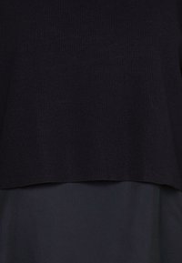 Czarny prążkowany sweter z dzianiny, nałożony na gładki czarny materiał, ukazujący kontrast faktur i prosty dół.