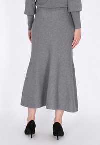 Jupe tricotée grise avec un ourlet évasé, un tissu texturé et une longueur au mi-mollet, assortie à des chaussures à talons hauts noires.