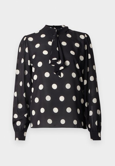 Μαύρο μπλουζάκι με λευκές πουά, ψηλός λαιμός και λεπτομέρεια δέσιμου. Μακριά μανίκια με σούρες στις μανσέτες, λεία υφή σατέν.