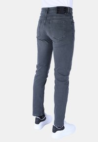 Grijze denim skinny jeans met achterzakken, subtiele vervaging en een gladde textuur. Gepaard met witte sneakers met zwarte accenten.