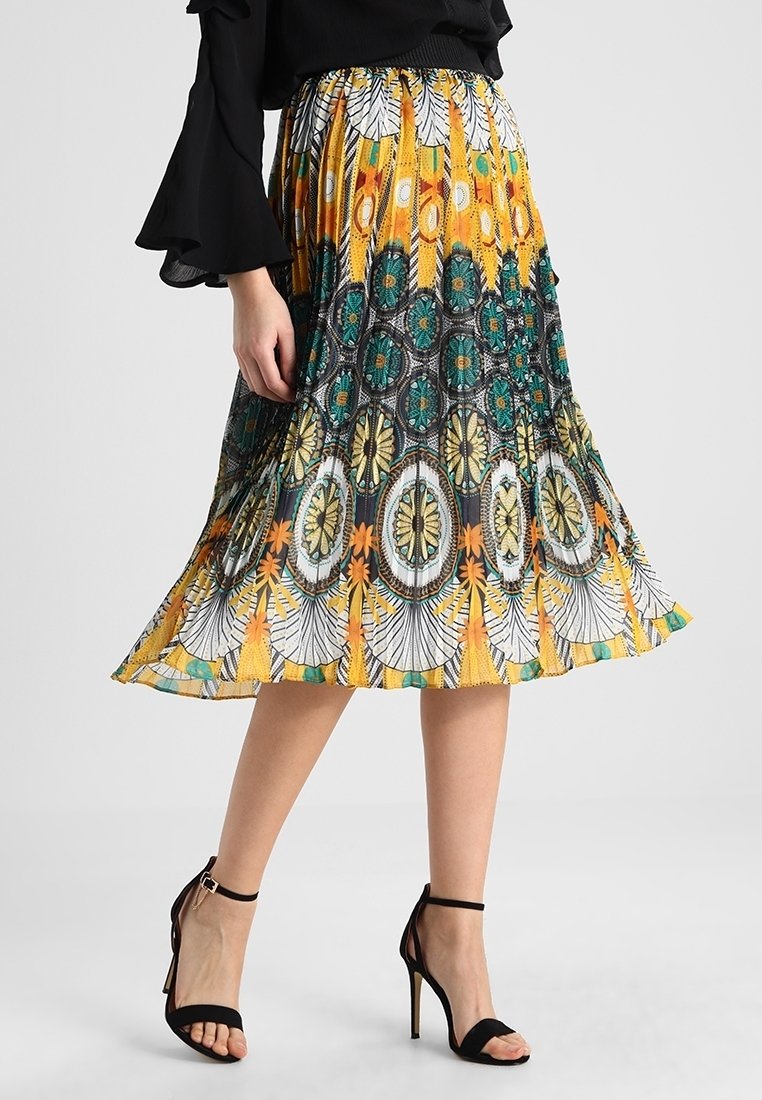 Femme portant une jupe midi colorée avec des motifs géométriques et floraux, associée à des sandales noires à talons hauts et un haut noir.