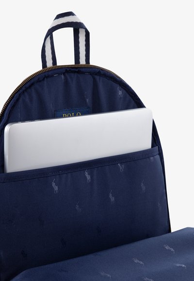 Donkerblauwe rugzak met een gladde textuur, met een ritsvak waarin een zilveren laptop is opgeborgen. Inclusief een gestreepte handgreep bovenaan en een subtiel logo-patroon.