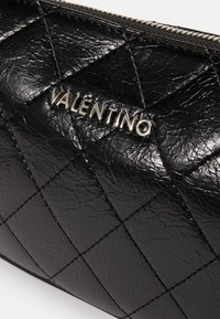 Quiltana črna usnjena torbica z oznako "Valentino" v srebrni barvi, z lesketajočo teksturo in izrazitim diamantom vzorcem.