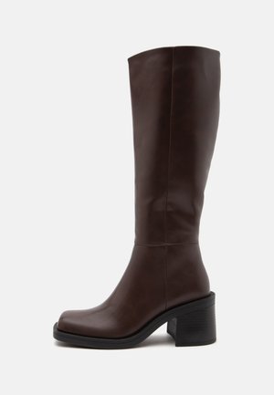 Botte en cuir marron foncé montant jusqu'au genou avec un bout carré arrondi et un talon épais sur fond blanc.