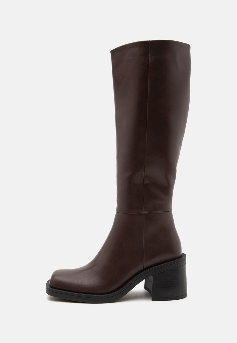 Botte en cuir marron foncé montant jusqu'au genou avec un bout carré arrondi et un talon épais sur fond blanc.