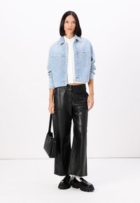 Giacca di jeans leggera blu con una vestibilità rilassata, abbinata a pantaloni larghi in pelle nera. Gli accessori includono una piccola borsa nera e scarpe chunky.