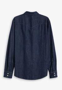 Camisa de mezclilla oscura con mangas largas, un cuello puntiagudo y puños abotonados. Presenta un detalle de yugo en la parte trasera y un dobladillo curvado.