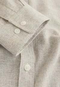 Camicia beige chiaro con bottoni, realizzata in tessuto strutturato con un delicato motivo a griglia e bottoni bianchi sui polsini.