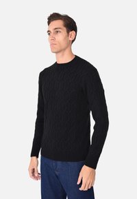 Maglione nero a maglia con un motivo esagonale testurizzato, colletto rotondo e polsini a coste, abbinato a jeans di denim blu.