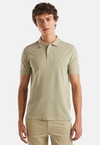 Polo de color verde claro, hecho de algodón texturizado, con cuello clásico, mangas cortas y un pequeño logo bordado en el pecho.