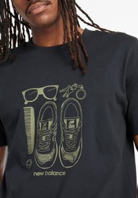 Camiseta negra con ilustración gráfica de zapatillas, gafas de sol y un peine en verde claro. Incluye el texto "new balance" en la parte inferior.