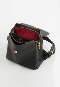 Bolso de cuero negro texturizado con herrajes dorados, con un interior de rayas rojas, bolsillo con cremallera y correa ajustable. Diseño de apertura superior.