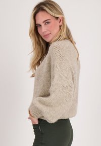 Lichtbeige gebreide trui met een losse pasvorm, ingewikkelde textuur, geribbelde manchetten en zijzakken, gecombineerd met donkergroene leggings.