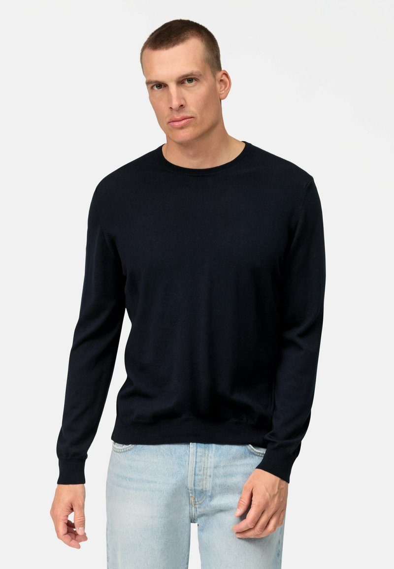 Maglione lungo a maniche per un morbido materiale di colore blu scuro, con scollatura rotonda e polsini a coste, abbinato a jeans blu chiaro.