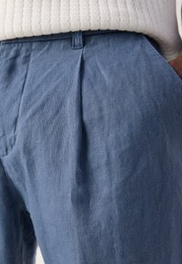 Pantaloni din in albastru deschis cu o finisare texturată, prezentând pliuri în față, buzunare laterale și o croială lejeră.