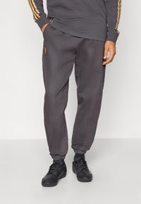 Grå joggerbyxor i tyg med elastiska muddar, utrustade med sidoseams och en liten broderad design på vänster lår.